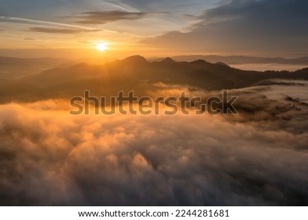 Sunny sunrise in autumn mountains. Mountains in a fog illuminated by rising sun. Autumn landscape with vivid sunlight.  Royalty-Free Stock Photo #2244281681