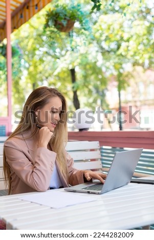 Vertical photo of a woman in working in front of laptop monitor. She looking at laptop monitor and smiling while sitting in summer cafe. Modern technology in every day life concept.