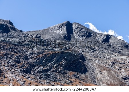 Shot of completely black granite slopes and peak with a matte reflection against pale blue sky and contrasting white cloud in Gran Paradiso National Park. Aosta valley, Italy