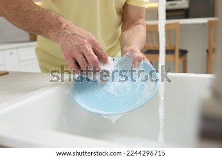 Closeup of man washing plate above sink in kitchen, view from outside Royalty-Free Stock Photo #2244296715