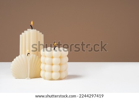 Handmade olive wax different forms burning candle on a duotone brown and white background. Sustainability vegan candle, natural materials. Minimalistic, cozy atmosphere modern photo.Copy space.Banner Royalty-Free Stock Photo #2244297419