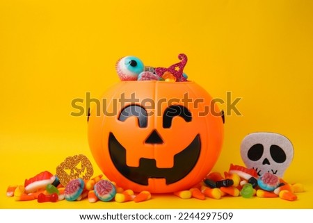 Halloween trick or treat bucket with different sweets on yellow background