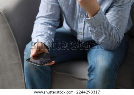 Man holding damaged smartphone while sitting on armchair, closeup. Device repairing