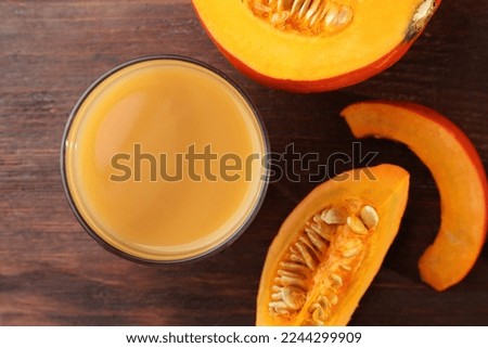 Tasty pumpkin juice in glass and cut pumpkin on wooden table, flat lay