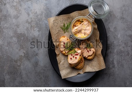 Plate with baguette toast with foie gras pate, directly above. A specialty food product made of the liver of a duck or goose,  in a glass jar. Decorated with red pepper and dill.