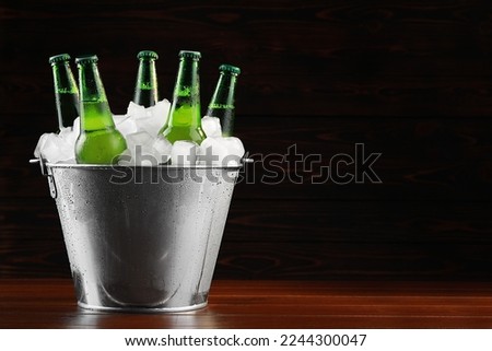 Metal bucket with bottles of beer and ice cubes on wooden background, space for text Royalty-Free Stock Photo #2244300047