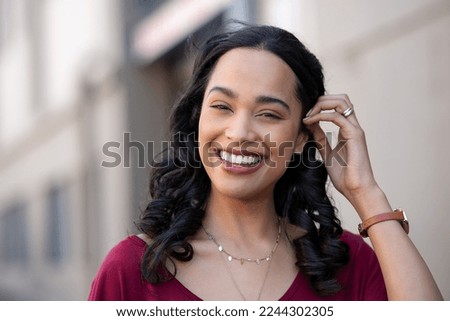 Happy young latin beautiful woman walking on city street. Portrait of carefree hispanic girl smiling and looking at camera. Joyful brazilian woman with long black hair smiling with copy space outdoor.