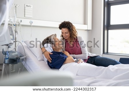 Lovely young daughter visiting old sick mother hospitalized in private clinic. Reassuring woman assisting her senior ill mother lying on hospital bed and talking. Senior and parent care concept. Royalty-Free Stock Photo #2244302317