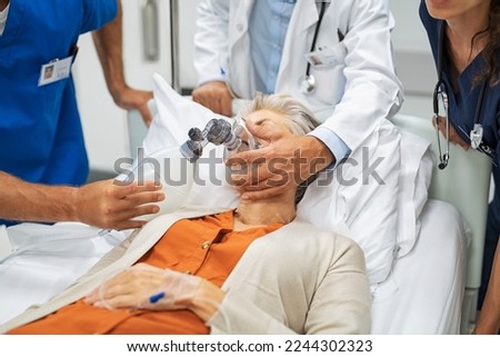 Doctors putting an oxygen mask on patient while rushing to operation theatre. Close up of nurse hand pumping oxygen in ambu bag mask during emergency. Team of emergency medical staff rescuing patient. Royalty-Free Stock Photo #2244302323