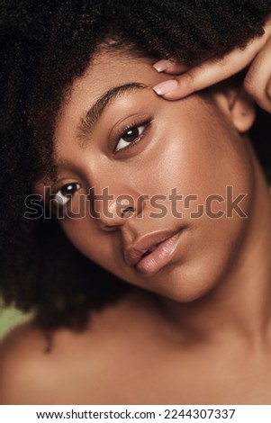 Young black woman with bare shoulders and Afro hairstyle touching eyebrow and looking at camera during spa session Royalty-Free Stock Photo #2244307337