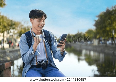 Asian man traveller using smart phone while sitting in the city park on beautiful day. Travel, vacation and journey concept