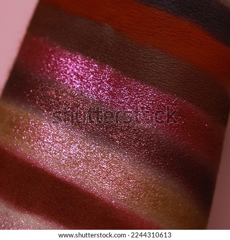 Eye shadow swatches, dry powder, set of cranberry red matte and metallic brush strokes on skin. Cosmetic makeup texture samples, smear trace samples on pink background. Realistic photography