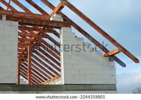 A timber roof truss in a house under construction, walls made of autoclaved aerated concrete blocks, a rough window opening, a reinforced brick lintel, blue sky in the background Royalty-Free Stock Photo #2244318801