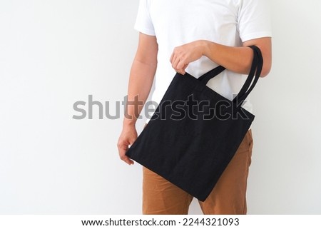 Young man hand holding black canvas tote bag on white background. Reusable eco bag for shopping. Eco friendly concept. Mockup for you designs.