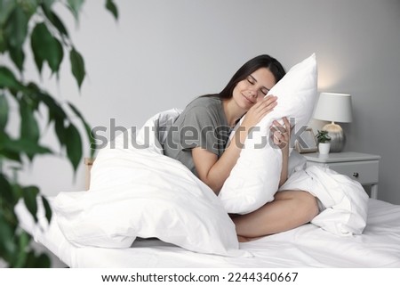 Beautiful young woman hugging pillow on bed at home Royalty-Free Stock Photo #2244340667