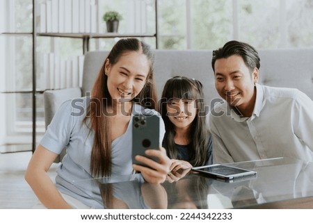 Cheerful asian family smiling enjoy taking selfie photo or video call at home, Dad mom and daughter sitting taking photo together in living room
