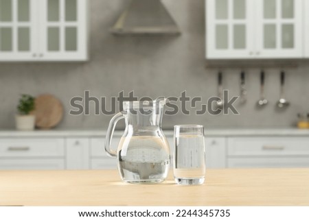 Glass and jug with water on wooden table in kitchen Royalty-Free Stock Photo #2244345735