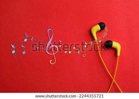Staff with music notes and treble clef flowing from yellow earphones on red background, top view