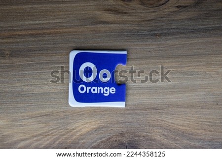 Puzzle piece with letter o and orange on it placed on wooden background.