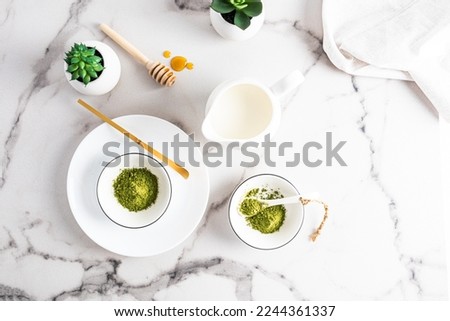 Green natural matcha tea powder in white ceramic bowls to prepare a healthy drink. top view. marble background.