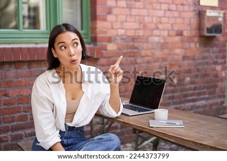 Enthusiastic asian woman, pointing at upper right corner, showing advertisement, news on banner, looking impressed and intrigued by smth.
