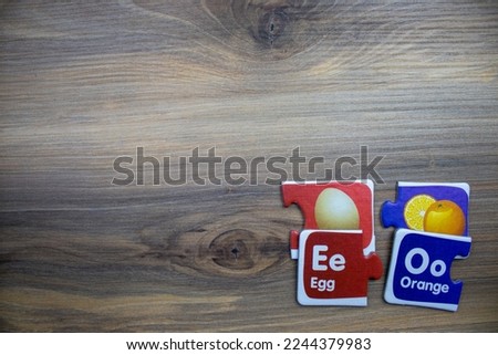 Puzzle pieces with pictures of eggs, oranges and the words egg, orange, placed on the right of a wooden background