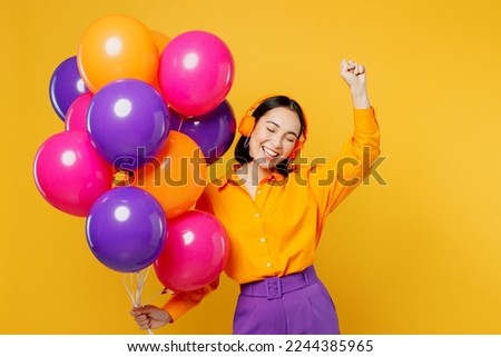 Happy fun young cheerful woman wears casual clothes headphones listen to music raise up hand dance celebrating hold balloons isolated on plain yellow background. Birthday 8 14 holiday party concept