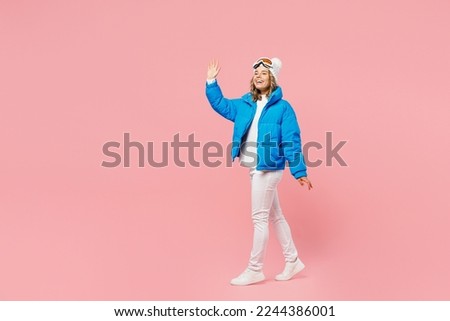 SIde view fun snowboarder woman wear blue suit goggles mask hat ski padded jacket walking go waving hand isolated on plain pastel pink background. Winter extreme sport hobby weekend trip relax concept
