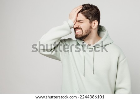 Young displeased sad unshaven caucasian man wear mint hoody put hand on face facepalm epic fail mistaken omg gesture isolated on plain solid white background studio portrait. People lifestyle concept Royalty-Free Stock Photo #2244386101