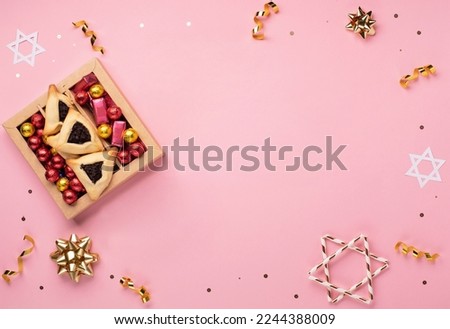 Purim celebration jewish carnival holiday card. Tasty homemade hamantaschen cookies, noisemaker, sweet candies and party decor on pink background, Top view. Happy Purim concept.