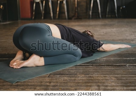 Photo from behind of a female new yoga teacher resting in child's pose (Balasana) with her arms extended during her vinyasa flow yoga practice alone and wearing sportswear indoors Royalty-Free Stock Photo #2244388561