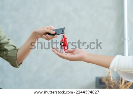 Real Estate agent with customer making contract signature giving a key buy. rent a house. Young lady taking keys from female real estate agent during meeting.