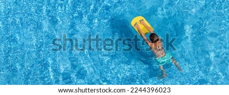 Boy child swim in swimming pool using board. Active wellness summer vacation in resort hotel. Water sports and game for children on summer holiday. Panoramic banner, copy space
