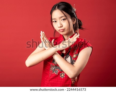 A 20-year-old Chinese Indonesian (Asian) girl in a Chinese traditional red dress (Cheongsam or Qipao), crossed her arm over one another to say no. Isolated on a red background.
