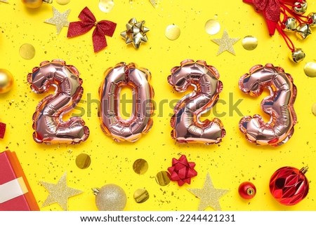 Figure 2023 made of balloons, Christmas decorations and confetti on yellow background