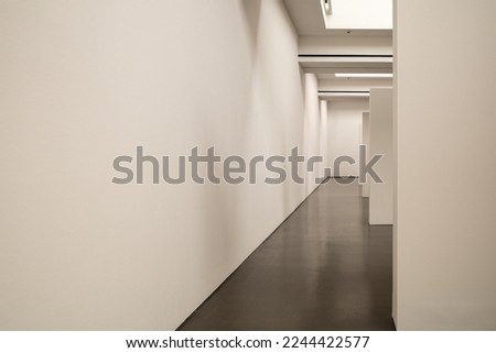 Interior diminishing perspective view of corridor between white wall and partitions inside gallery space.   Royalty-Free Stock Photo #2244422577