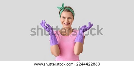 Portrait of beautiful housewife wearing rubber gloves on light background Royalty-Free Stock Photo #2244422863