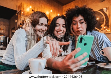 Group of young women having fun sharing media with an cellphone. Three girls looking to the smartphone on a coffee shop, restaurant or bar. Female students buying on a market place using a mobile Royalty-Free Stock Photo #2244436405