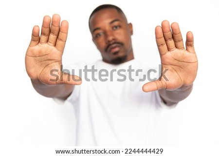 Dissatisfied African American man showing open palms. Hands of serious young male model with short hair and beard in white T-shirt looking at camera, showing stop sign. Restriction, refusal concept
