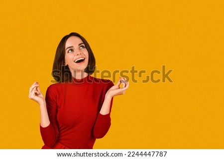 Dreamy excited beautiful brunette young woman in red snap fingers and looking at copy space over orange studio background, making dreams come true, waiting for mirracle Royalty-Free Stock Photo #2244447787