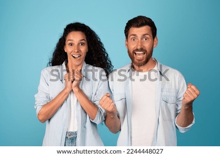 Satisfied excited surprised young european male and arab lady make sign of victory and success with hands, isolated on blue background, studio. People emotions from victory, excellent ad and offer