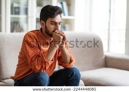 Permacrisis, life problems, financial hangout concept. Pensive young middle eastern man sitting on sofa at home, leaning on his hands, experiencing difficulties in life, looking at copy space Royalty-Free Stock Photo #2244448085