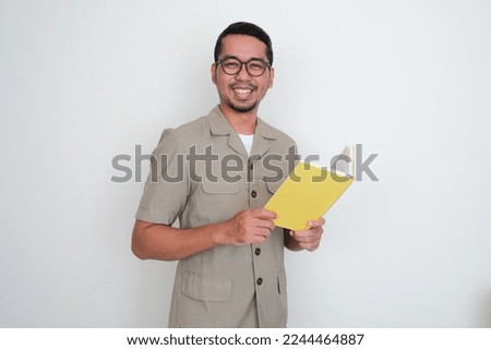Young Indonesian teacher smiling happy at the camera while holding a book Royalty-Free Stock Photo #2244464887