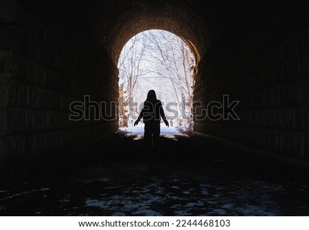 View of silhouette of woman standing in dark tunnel  in winter; snow covered trees in background 
