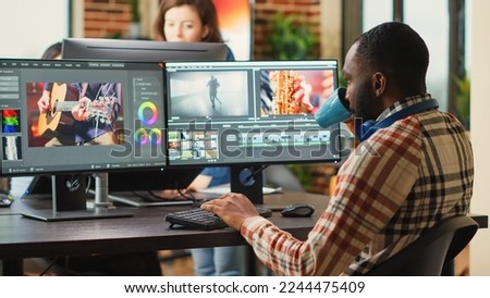 African american employee editing video content on multimedia software, using focus lighting and color grading. Male filmmaker working on movie montage edit on pc multi monitors.