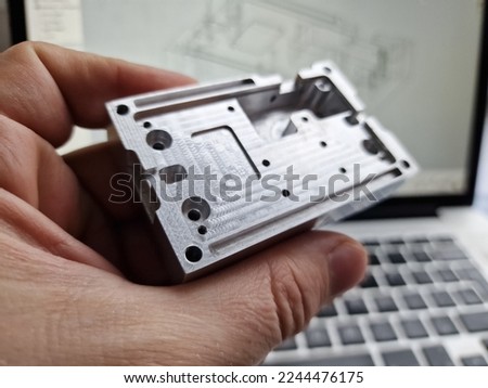 Mechanical engineer hand holding CNC milled custom designed project in front of computer screen and drawings Royalty-Free Stock Photo #2244476175