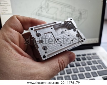 Mechanical engineer hand holding CNC milled custom designed project in front of computer screen and drawings Royalty-Free Stock Photo #2244476179