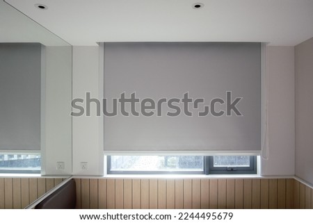 Roller blinds closeup on the window in the interior. Blackout roller shades for big windows. Chain control. Grey color, texture material. Sun protection and window decoration. Royalty-Free Stock Photo #2244495679