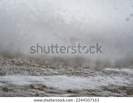 Blowing snow and Focus stacked ground level view of ice accumulation on a sidewalk with blowing snow.  Royalty-Free Stock Photo #2244507163