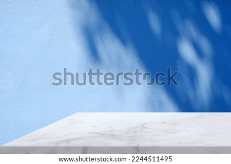 White Marble Table Corner with Light Beam, Shadow, and Spotlight on the Blue Concrete Wall Background, Suitable for Product Presentation Backdrop, Display, and Mock up. Royalty-Free Stock Photo #2244511495
